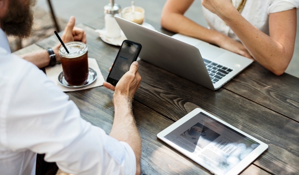 two people at table looking at phone and computer