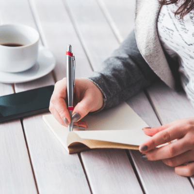 young adult female writing down financial advice in a notebook with coffee