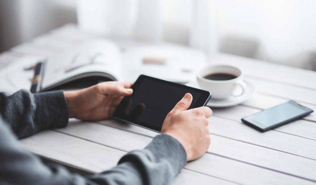 young adult holding a tablet at a table with coffee