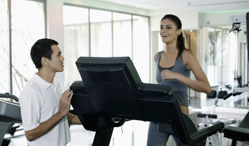 man working as a personal trainer for extra money, woman running on treadmill