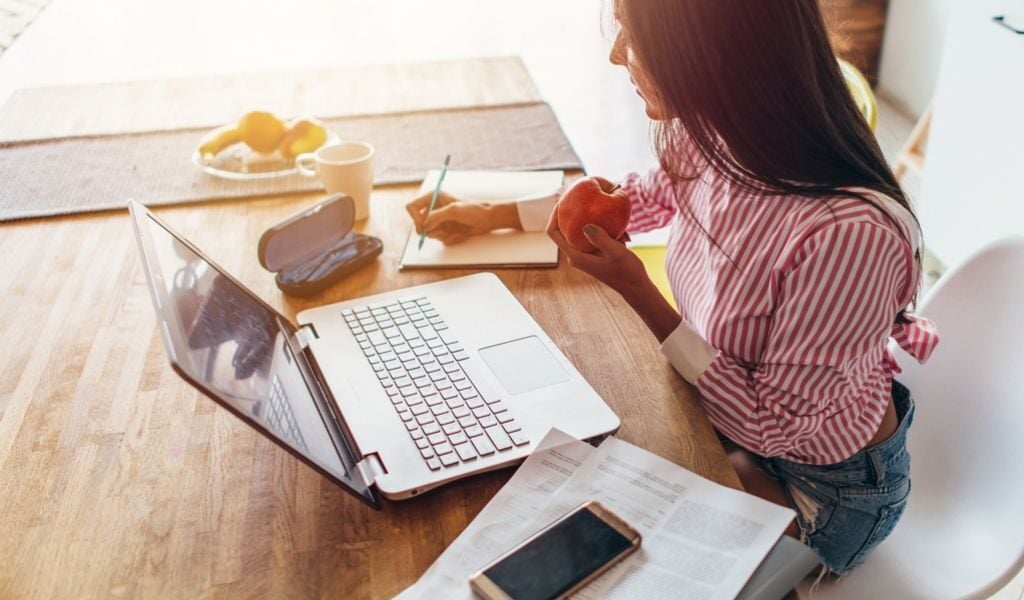 female at table looking at computer and writing