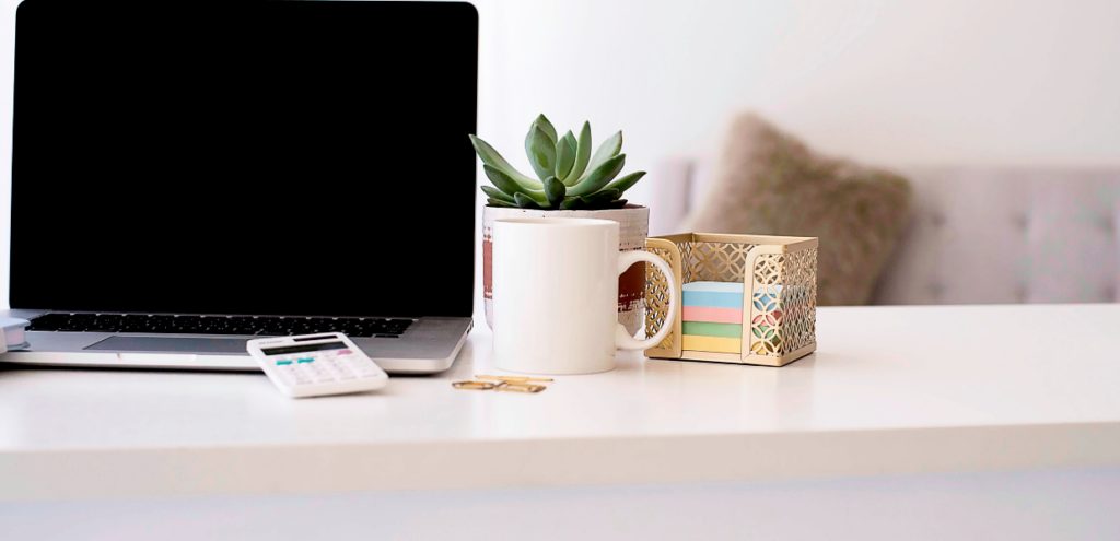 computer on white desk with coffee cup and office supplies