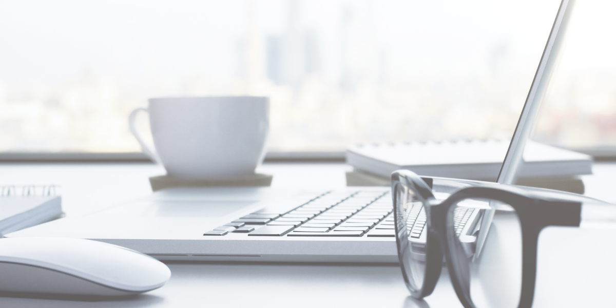 Pair of glasses sitting on desk with a computer, notebooks, and a cup of coffee