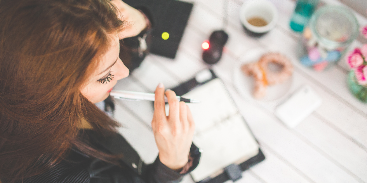 White female working at desk holding a pen to her mouth