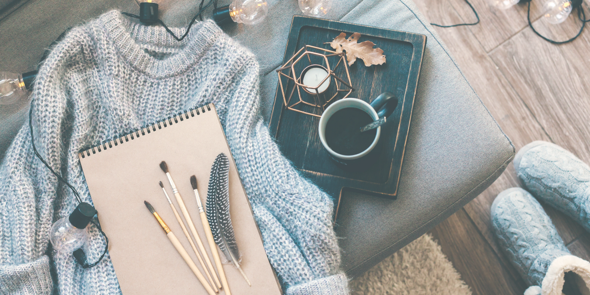 Soft gray sweater lying on an ottoman with a cup of coffee and a notebook 