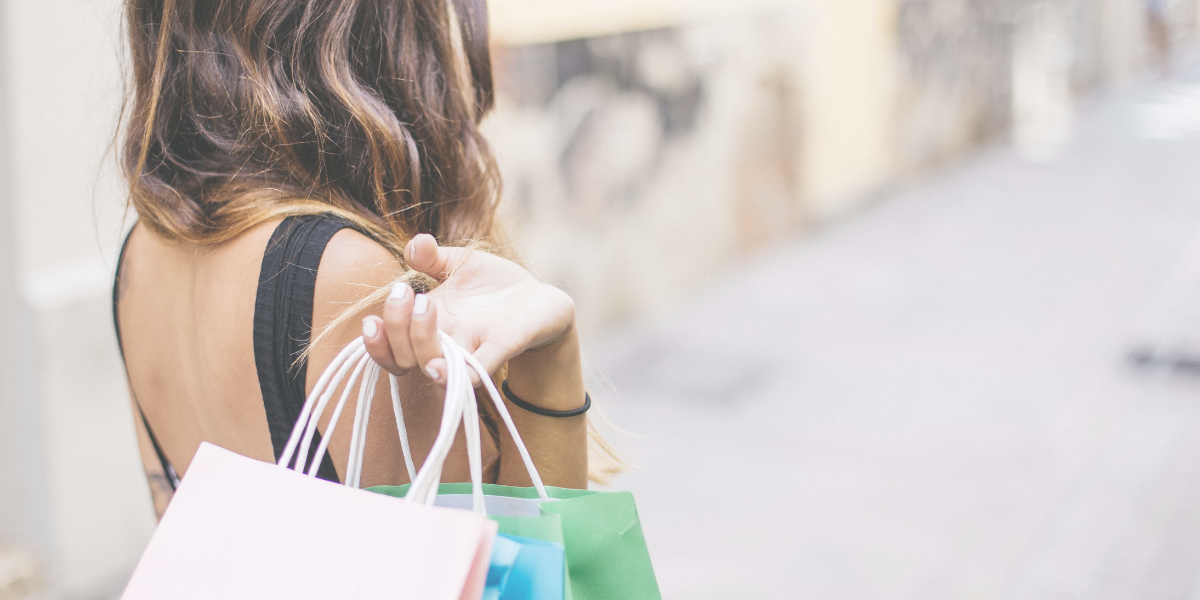 Female holding three paper shopping bags behind her as she walks.