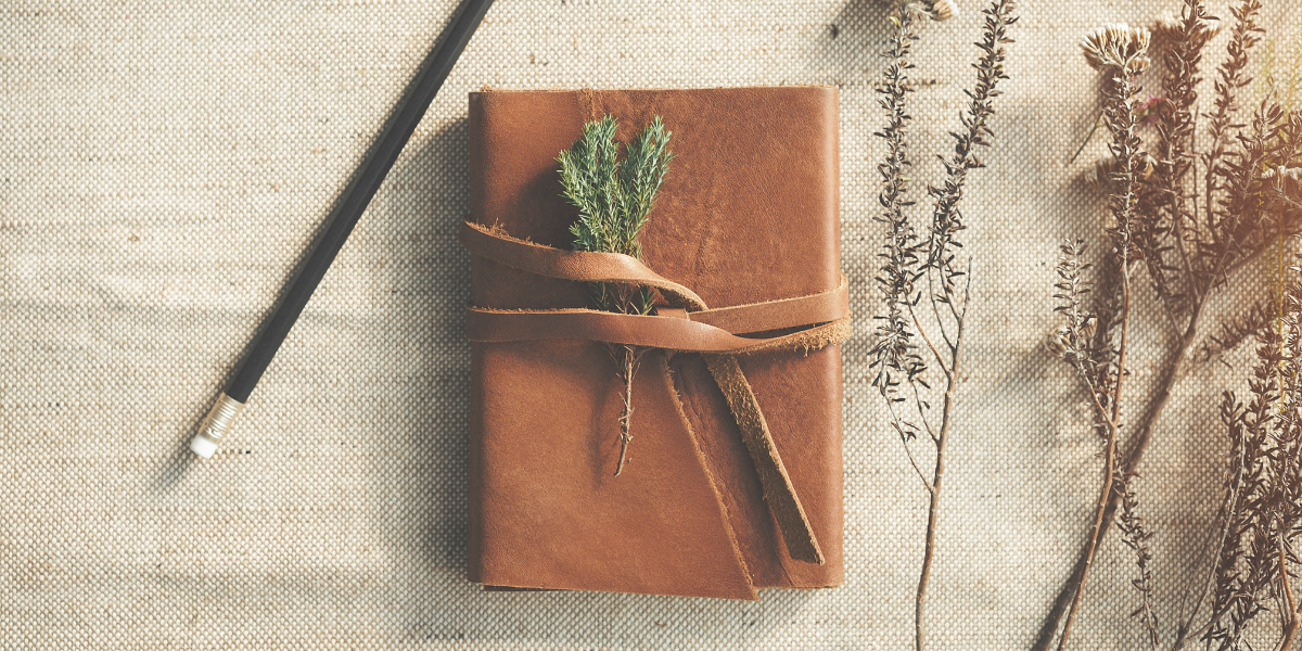 Brown leather journal with wildflowers lying beside it along with a pencil. 