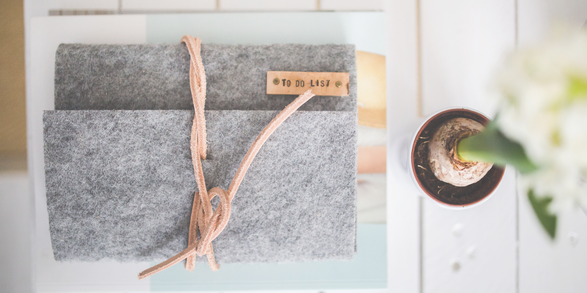 Grey clothe journal sitting on a desk with a flower sitting beside it