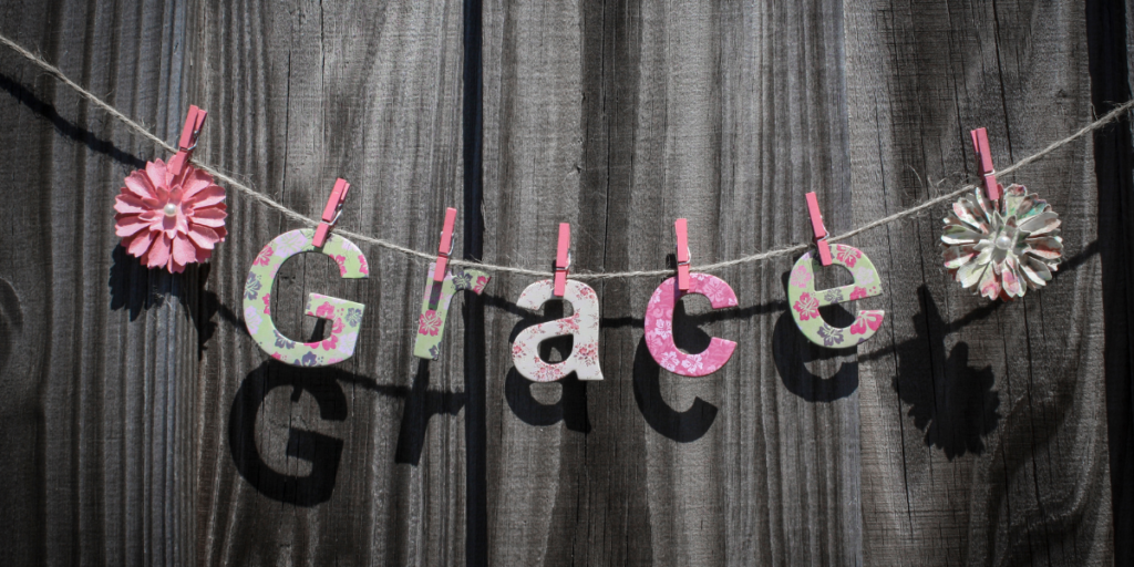 The word grace hanging from a string in front of a wood fence reminding us to give yourself some grace when working towards securing a financial future and changing ones money mindset. 