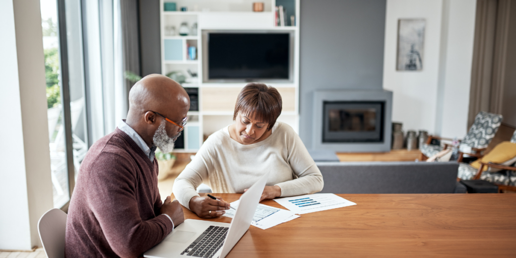 A couple sitting at the kitchen table reviewing paperwork and discussing their financial goals. 