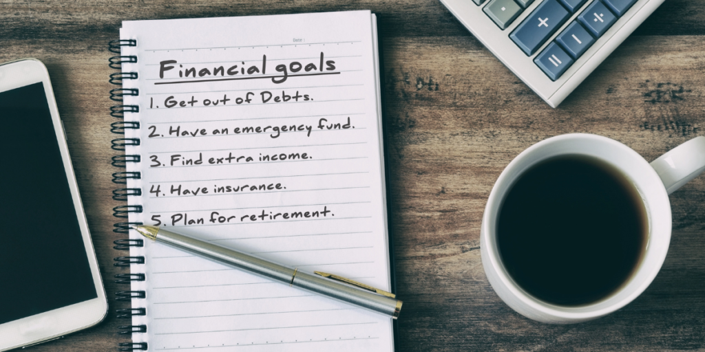 A cellphone, calculator, cup of coffee and a pen on a notepad with financial goals listed 1-5. 