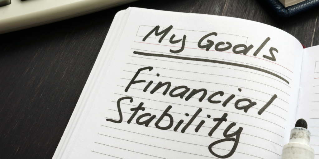 A notebook and a black marker that was used to write "My Goals. Financial Stability" on a piece of paper to reach financial goals. 