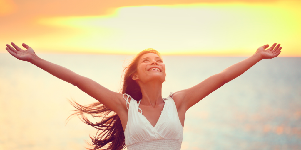 A female in front of a beautiful sunset realizing how good it feels to have financial security and reach her financial goals. 