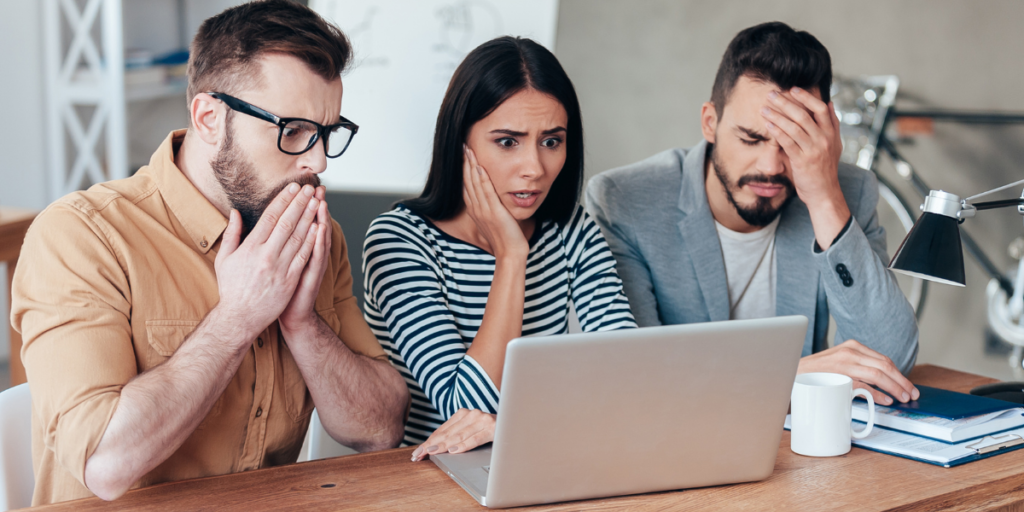 Two men and a woman looking at a laptop in shock that they did not stick to their budget. 
