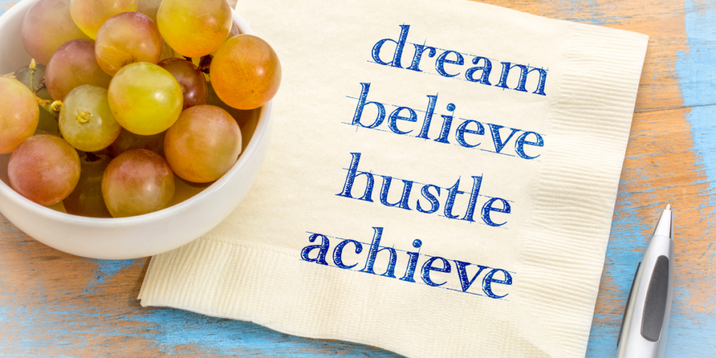 A small bowls of grapes sitting on a napkin with the words dream, believe, hustle, achieve for reaching financial goals. 