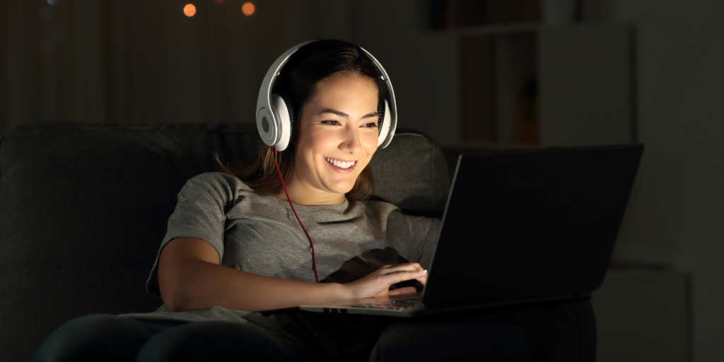 Lady wearing headphones and using her laptop to watch free movies online. 
