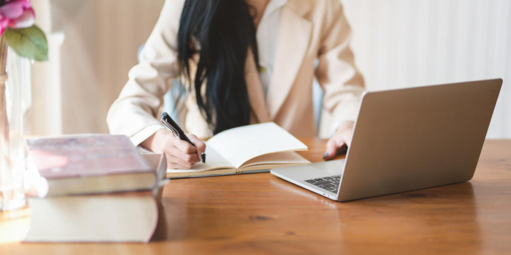 A female sitting at a table using her laptop to run her online business that helps people reach their financial goals. 