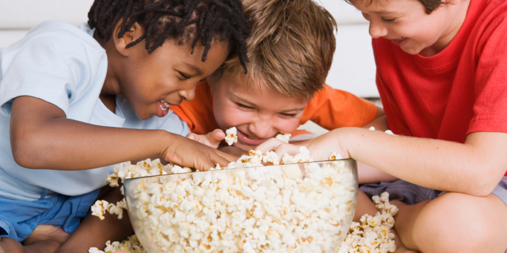 Three kids enjoying popcorn while watching free movies online. 