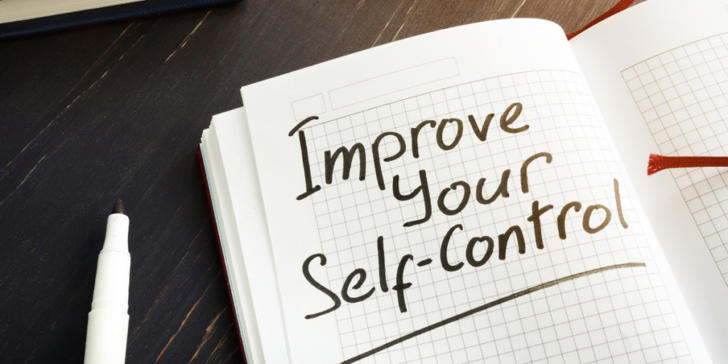 A grid notebook laying on a tabletop and a marker nearby with "Improve Your Self-Control" written on the page as a prompt for one to stick to their budget. 