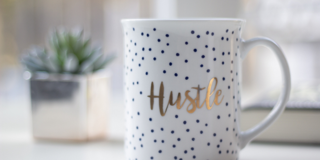 A white coffee mug with black polka dots with the word "Hustle" in gold lettering reminding us all to keep pushing and take those side hustle opportunities as they come. 