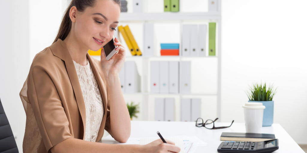 A woman talking on her phone and taking notes working part time as a personal assistant.