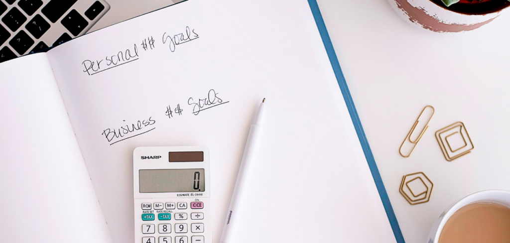 A blue notebook with written personal and business goals. On top is a calculator and a white pen.