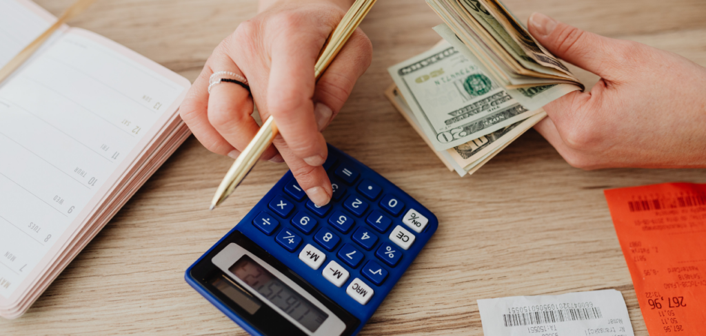 A woman calculating money and receipts using a blue calculator, a notebook and a pen