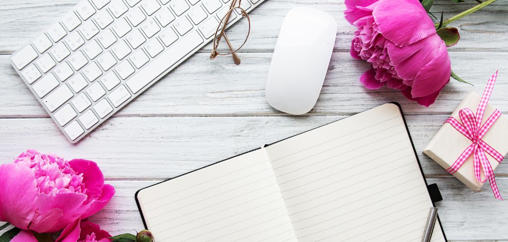 Keyboard, glasses, pink flowers, computer mouse, notebook and small gift box with pink ribbon. 