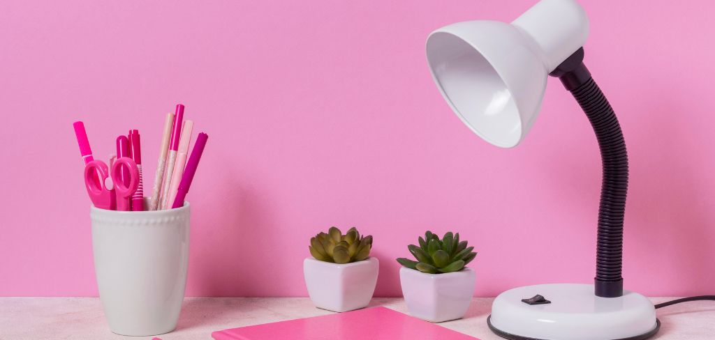 Pink wall with white desk lamp and white container with pink pens and scissors.  Two succulents.