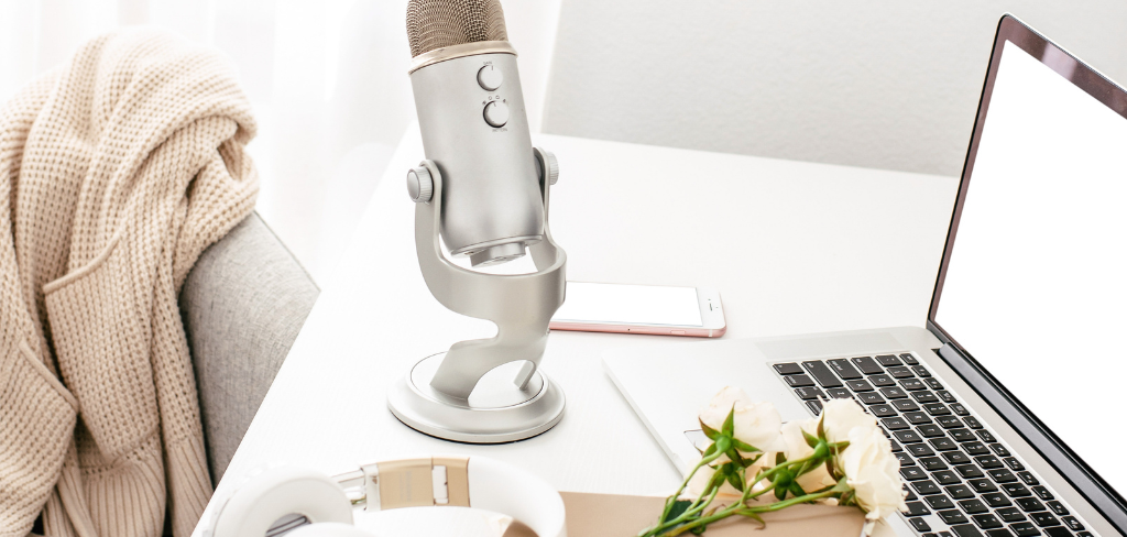 Microphone on desk, laptop with flowers and headphones.  Office chair with sweather.