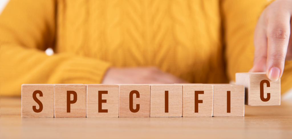 Female hand arranging wood letters and writing the word specific.