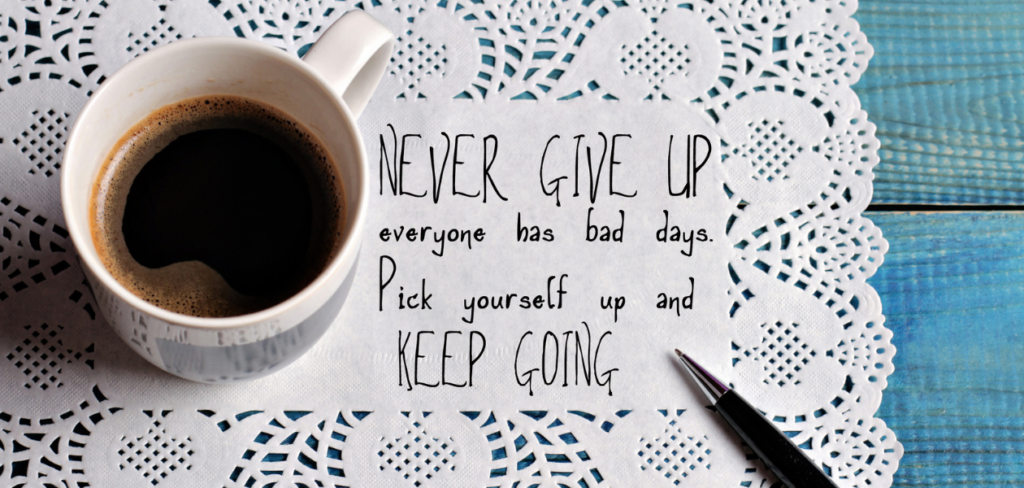Motivational quote, 'Never give up and keep going,' is written on a piece of paper and placed on top of a table next to a cup of coffee.