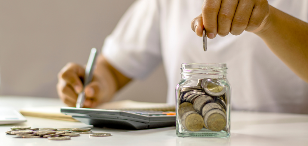 A person's hand is putting coins in a jar for saving money.