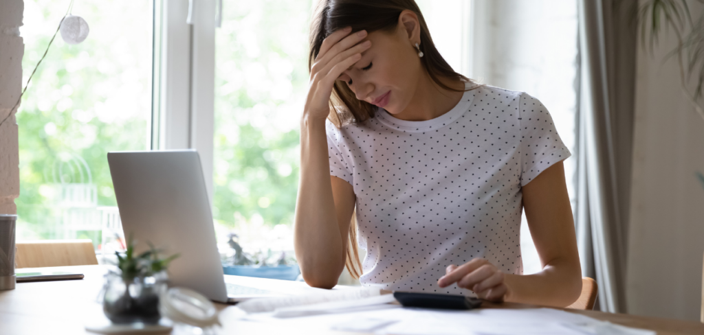 The frustrated woman is sitting at a desk with a laptop and a calculator.