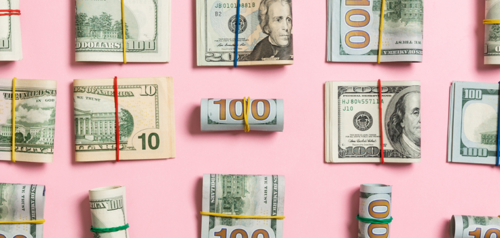 A pink background with different US dollar bills bundled together by a rubber band.