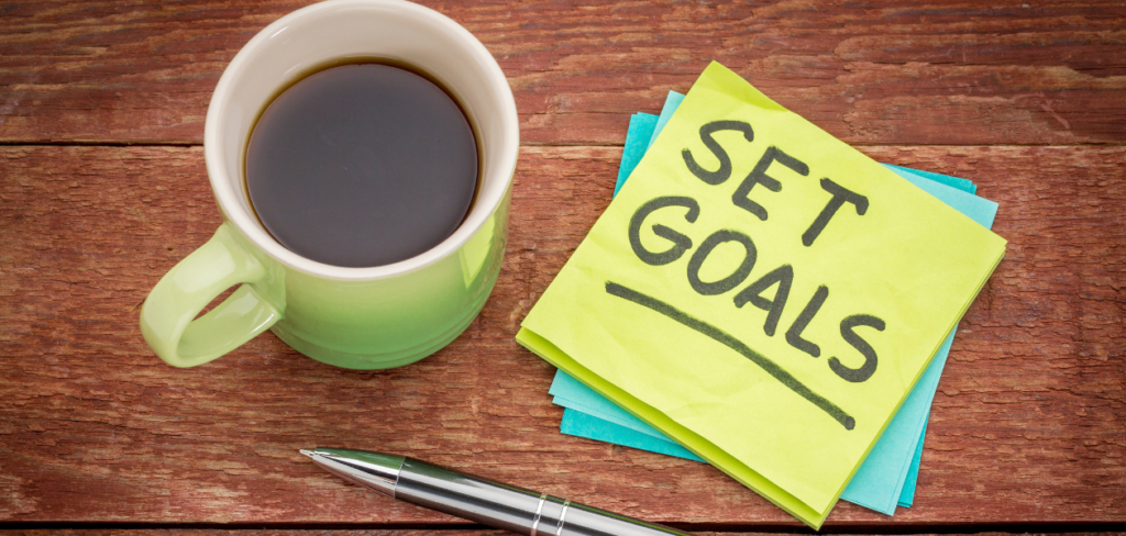 Set goals reminder on a sticky note with a pen and a cup of coffee.