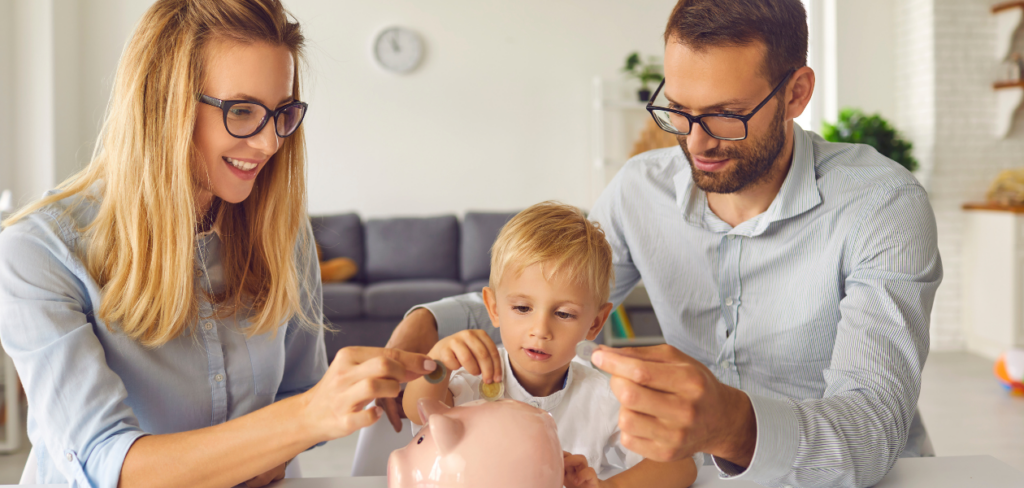 A kid is putting money inside a piggy bank and learning how to save money from his parents.