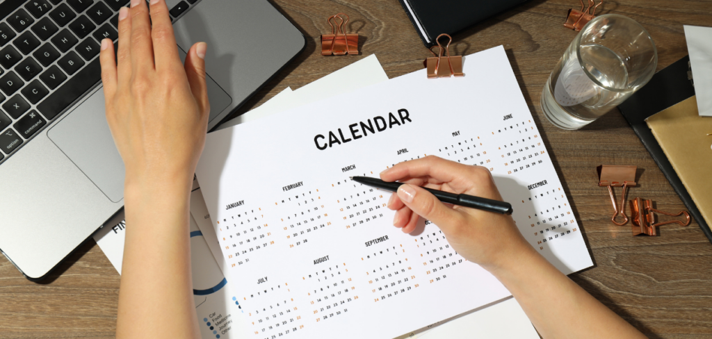 A hand browsing the laptop and writing on a desk calendar.