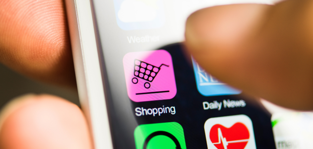Hand holding phone, shopping app on screen. Thumb touching app logo.