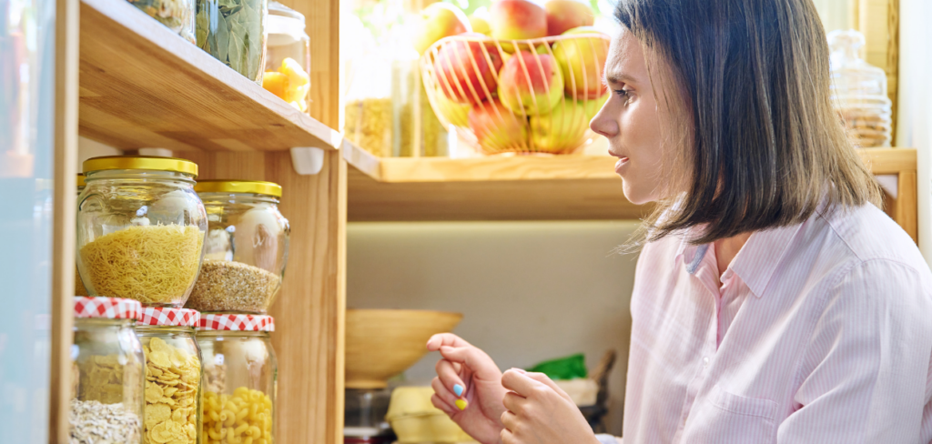 A woman in home pantry with container jars of cereals, pasta, dry fruits