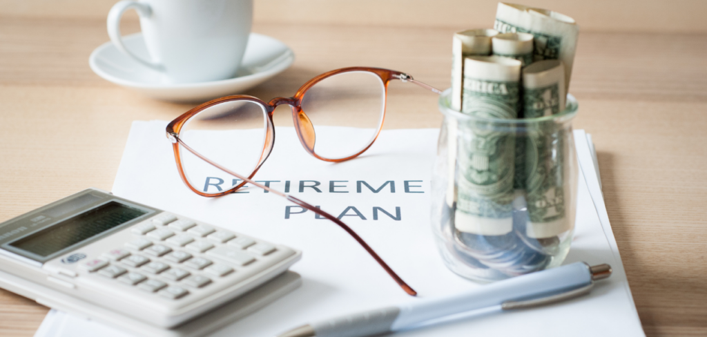 Retirement plan documents, pen, calculator, dollar bills and coins in a jar, eye glasses, and coffee mug on a table