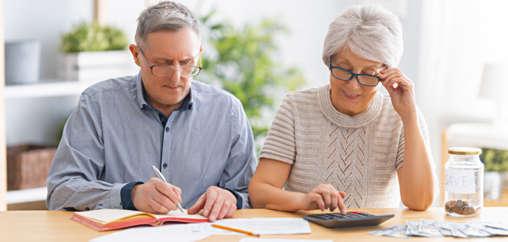 Elderly couple sitting at the desk with a paper receipt in hands are calculating expenses, managing the family budget.