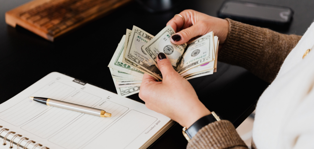 A notebook and a pen are on the table, and a person is counting money.