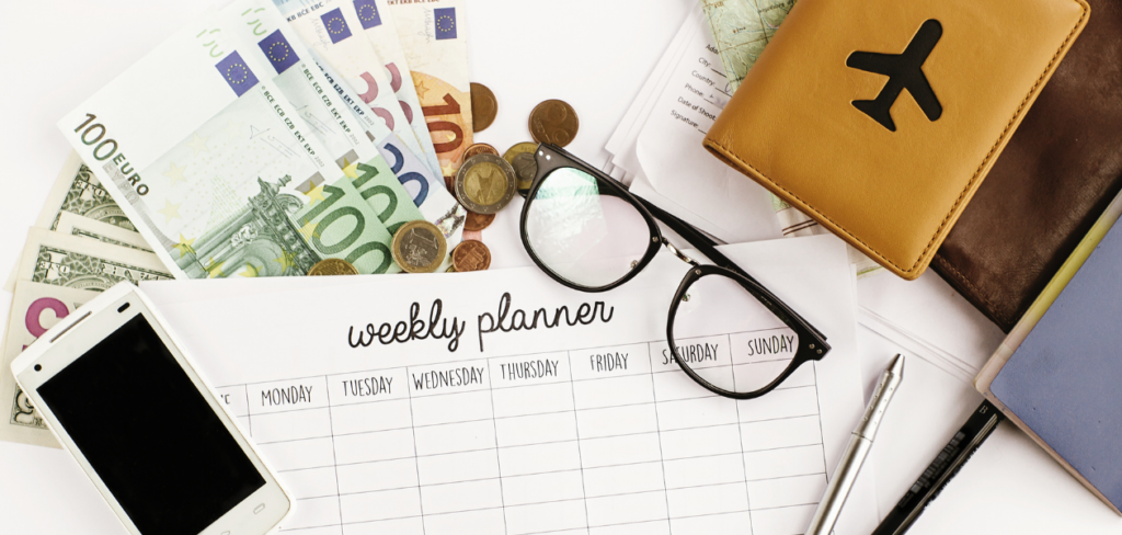 A weekly planner, money, mobile phone, eyeglasses, pen and passport holder on the table.