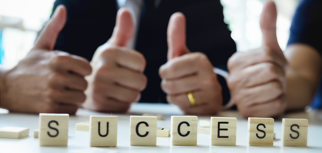 People showing thumbs up with the word success on wooden blocks in front of them.
