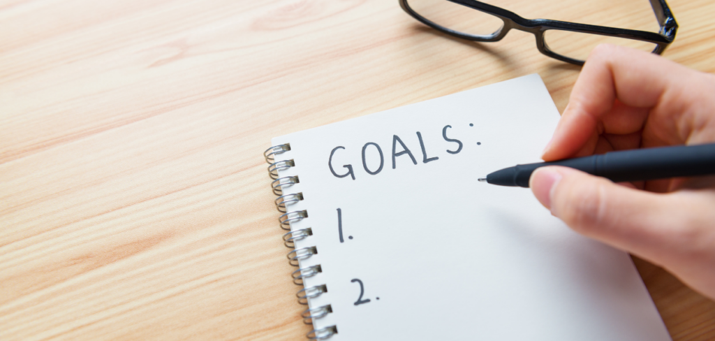 Hand writing goals in a notebook on a wooden table.
