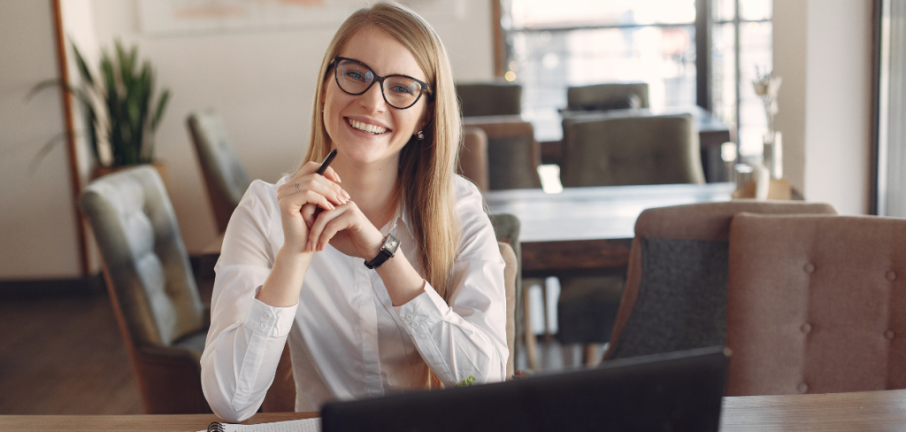 A financial advisor in glasses sitting at a table in the office with a laptop, pen and a notebook.
