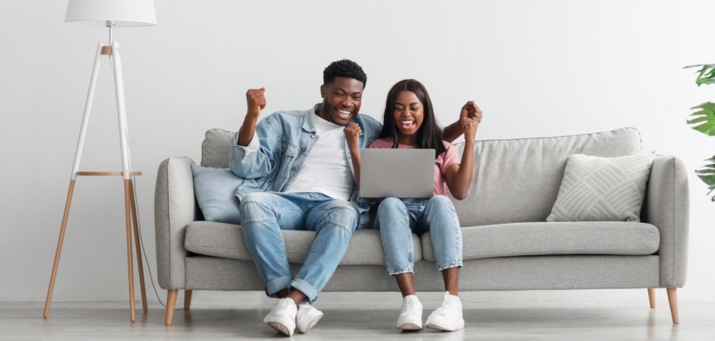 Couple sitting on couch with laptop celebrating.
