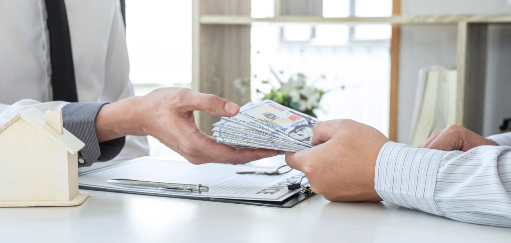 A man is handing some cash to the financial advisor for payment, and there is a contract on the table.
