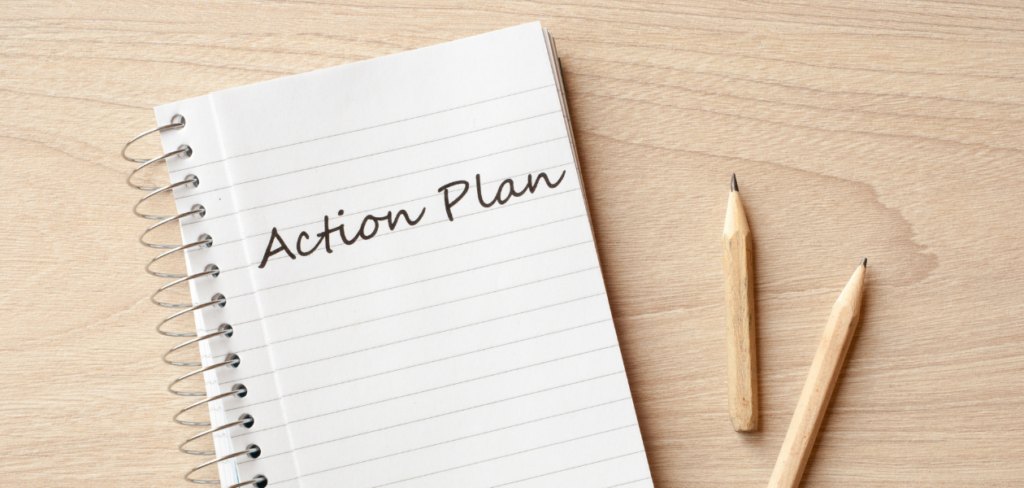 Notebook with action plan written on it and two pencils on a wooden table.